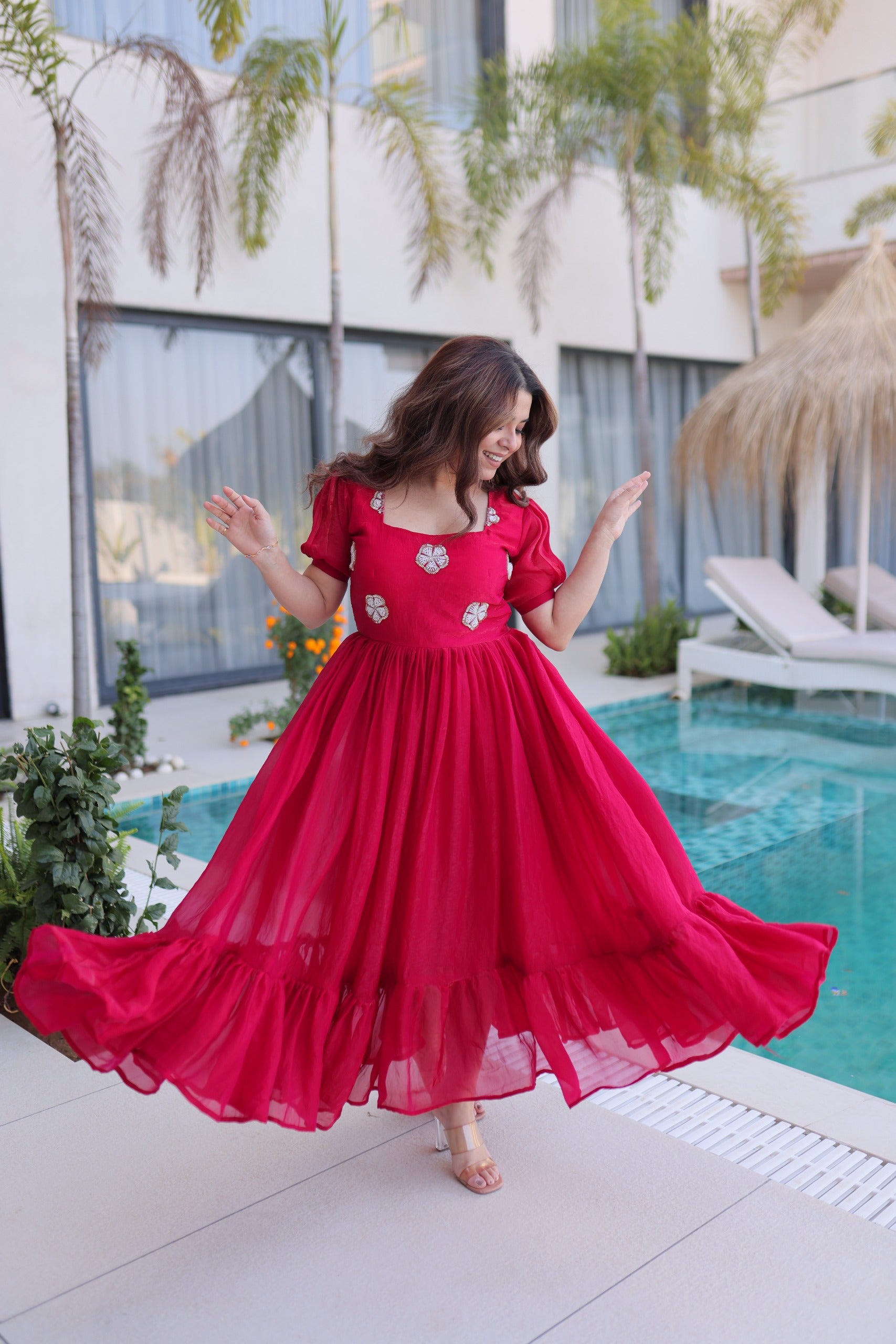 Woman in a pink dress standing by a pool with greenery and a building in the background