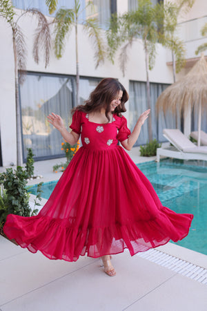Woman in a pink dress standing by a pool with greenery and a building in the background