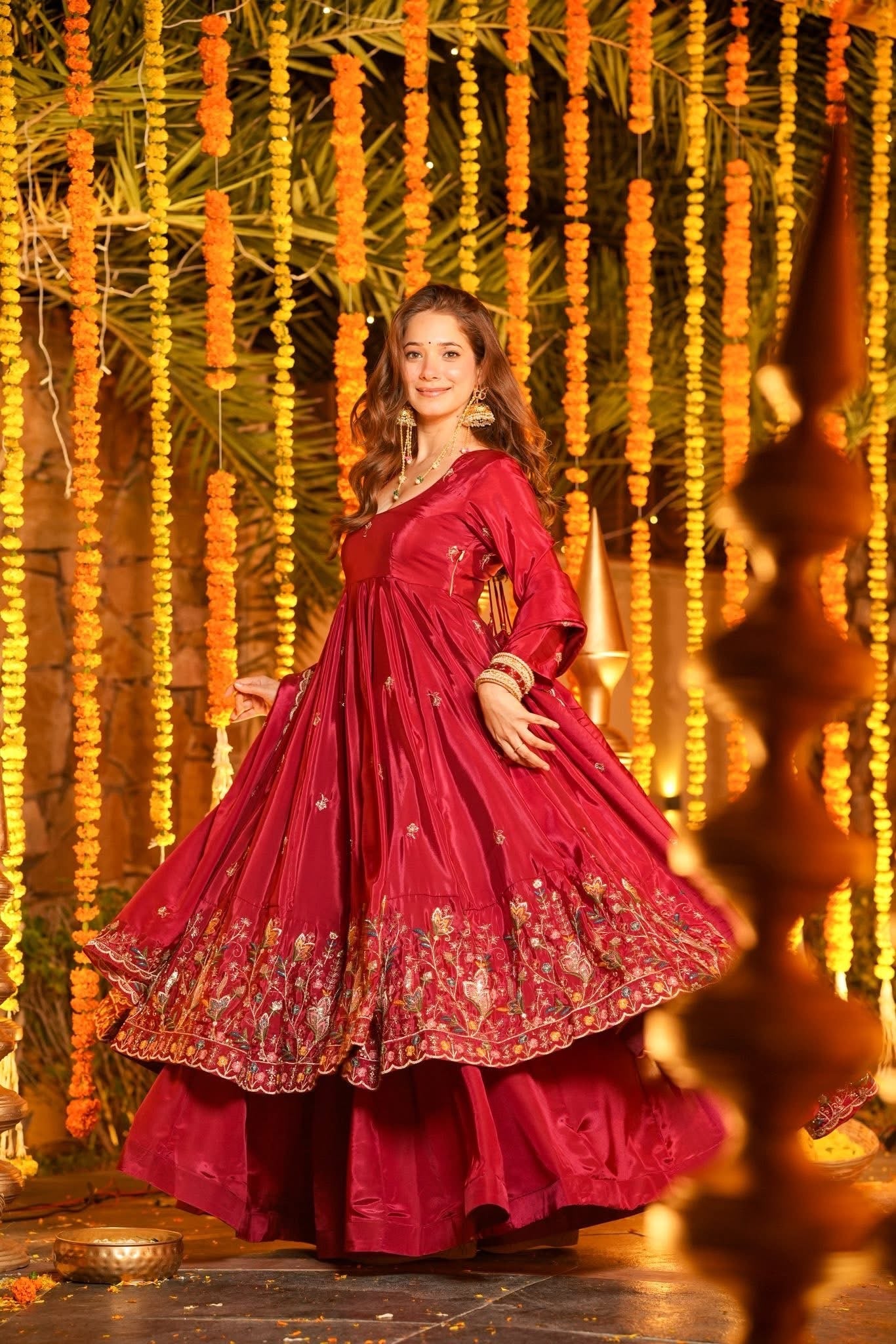 Woman in a red traditional outfit standing in front of decorative lights and flowers.