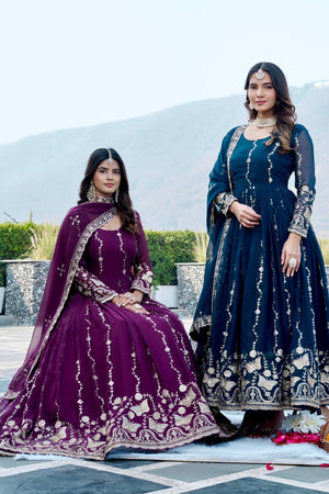 Two women in traditional outfits standing outdoors with a scenic background.