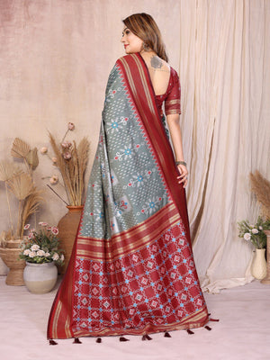 Woman wearing a red and gray saree with floral patterns in a decorated room.
