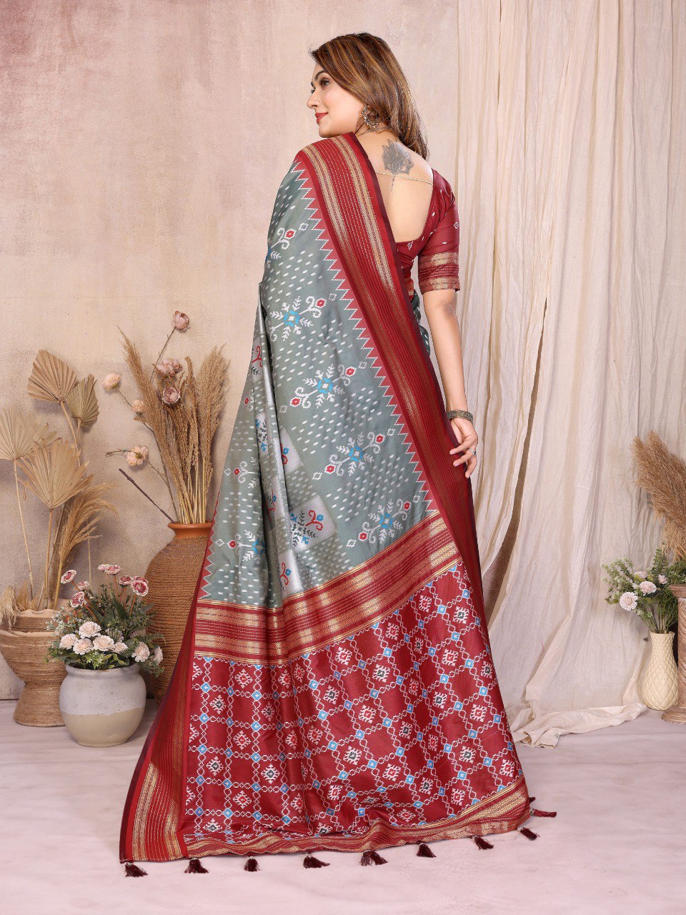 Woman wearing a red and gray saree with floral patterns in a decorated room.