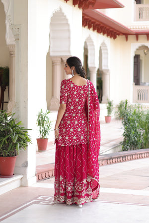 Woman in a red traditional outfit standing in a decorative outdoor setting with plants and architectural elements.