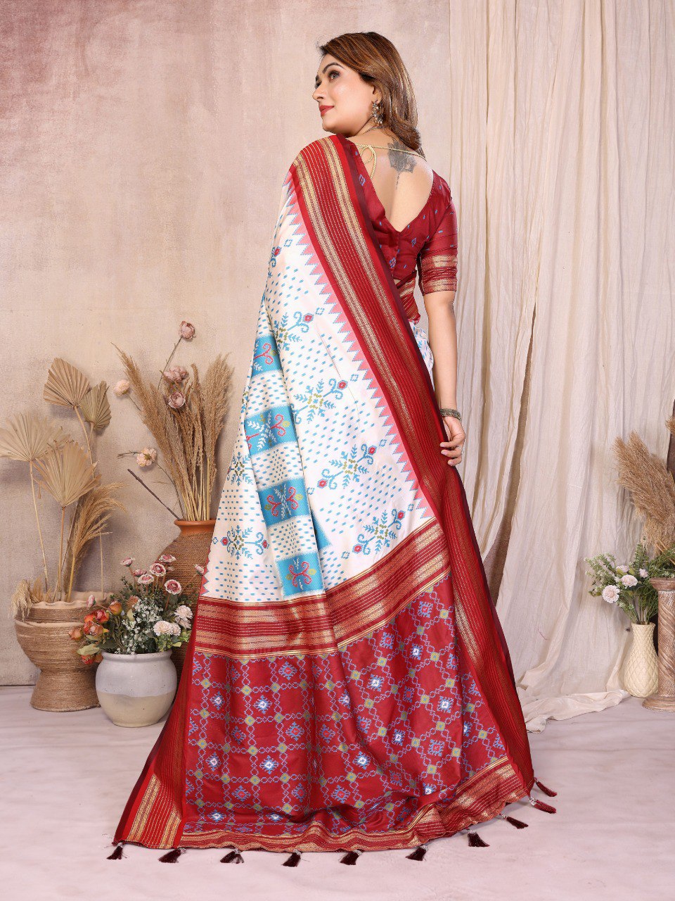 Woman wearing a red and white saree with floral patterns in a decorated room.