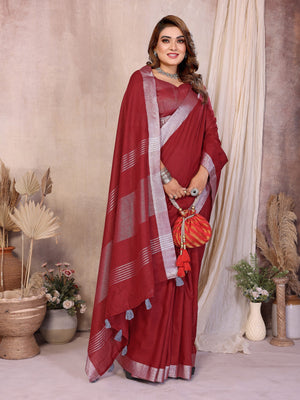 Woman wearing a red saree with a white border in an indoor setting with decorative plants.