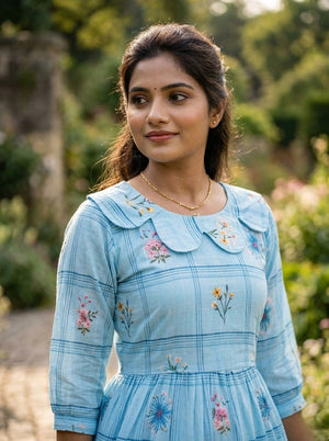Woman wearing a light blue dress with floral embroidery in an outdoor setting