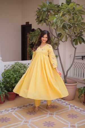 Woman in a yellow dress standing in a room with plants and decorative tiles.