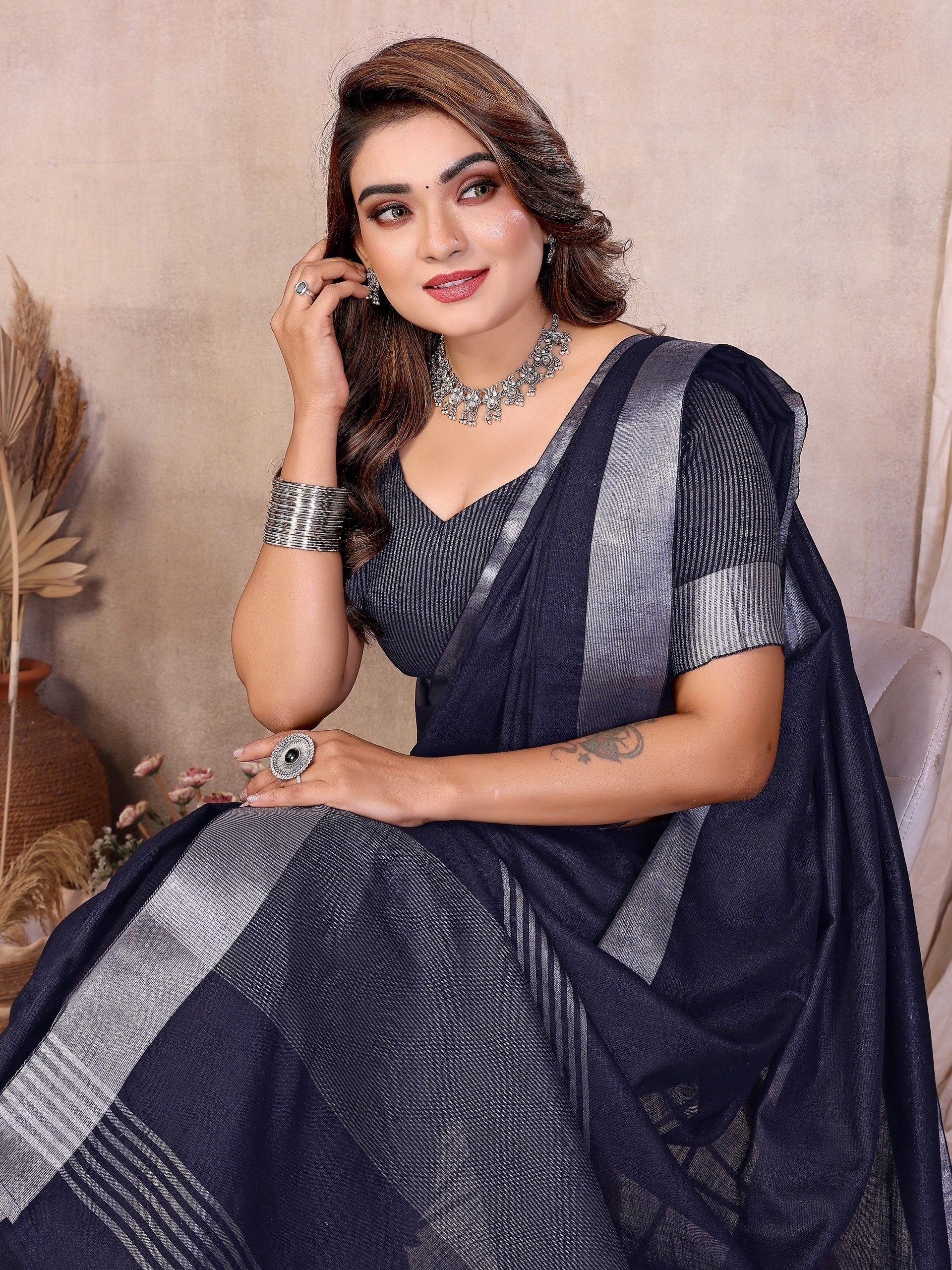 Woman wearing a dark blue saree with silver stripes, sitting against a neutral background.