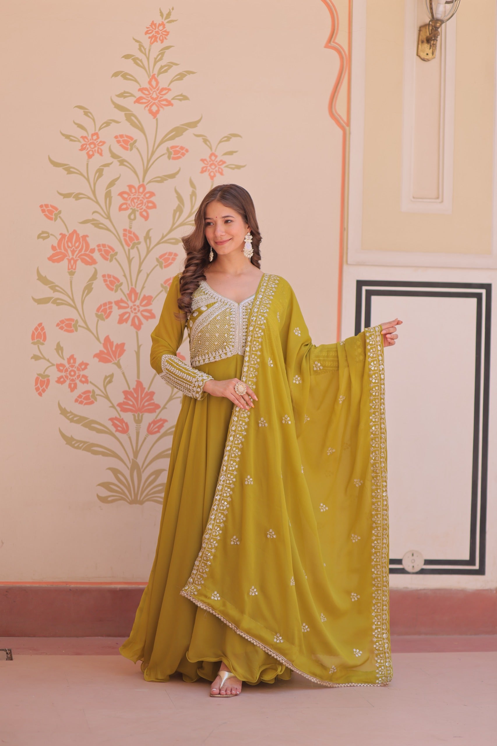 Woman in a green traditional outfit with a floral wall design in the background