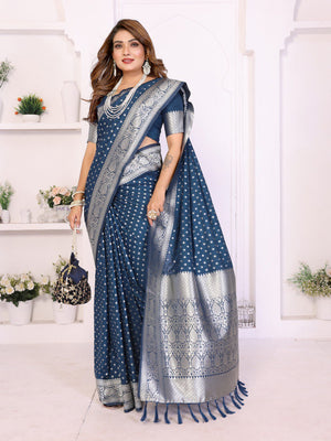 Woman wearing a blue saree with silver patterns in a white room.