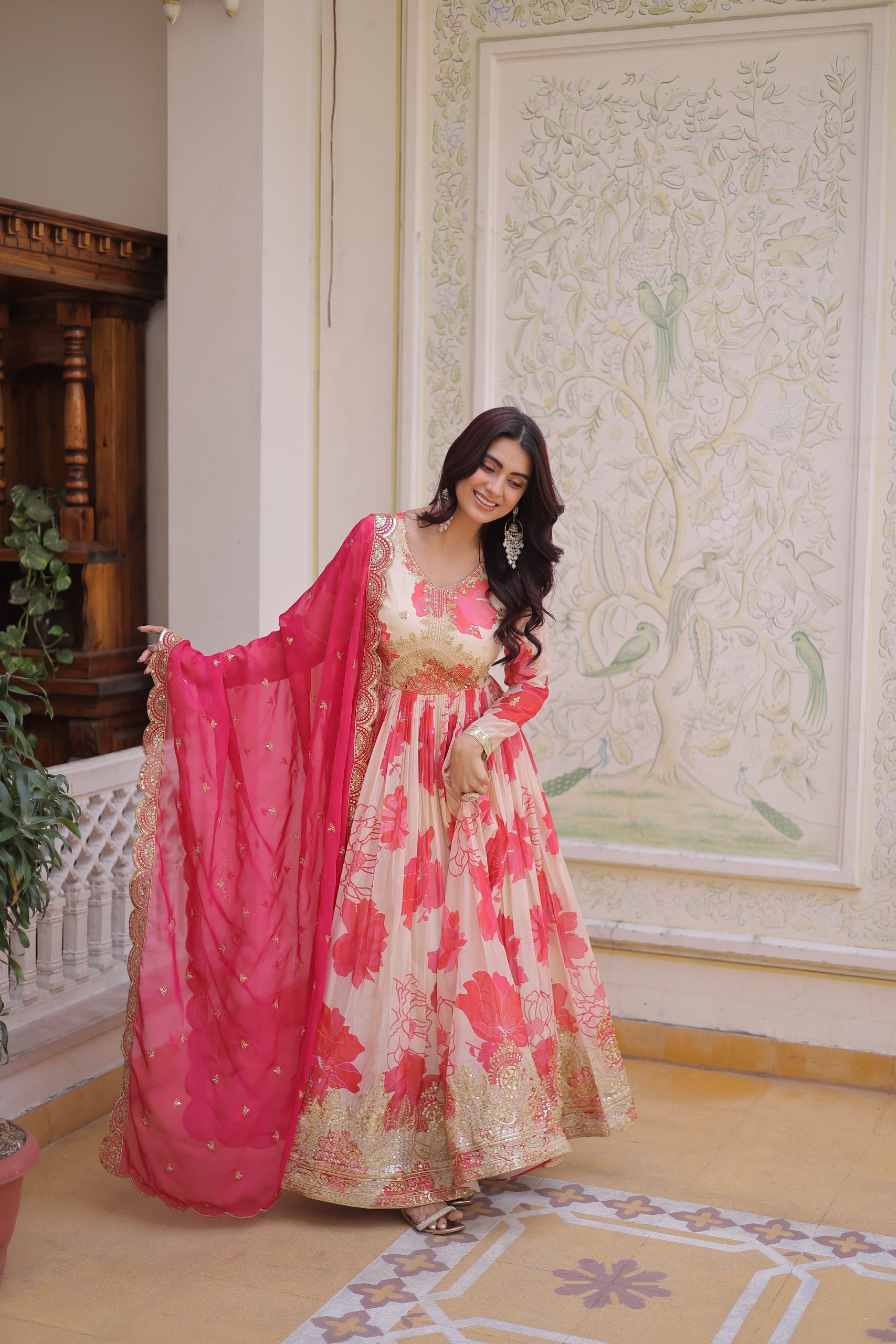 Woman in a floral dress with a pink dupatta standing in an ornate room.
