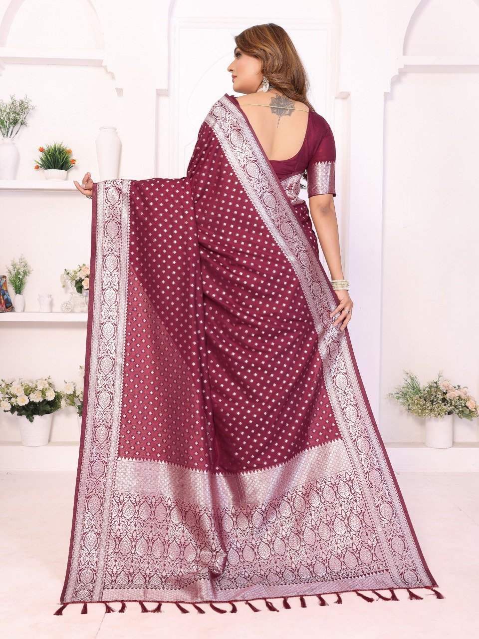 Woman wearing a maroon saree with white patterns in a bright room.