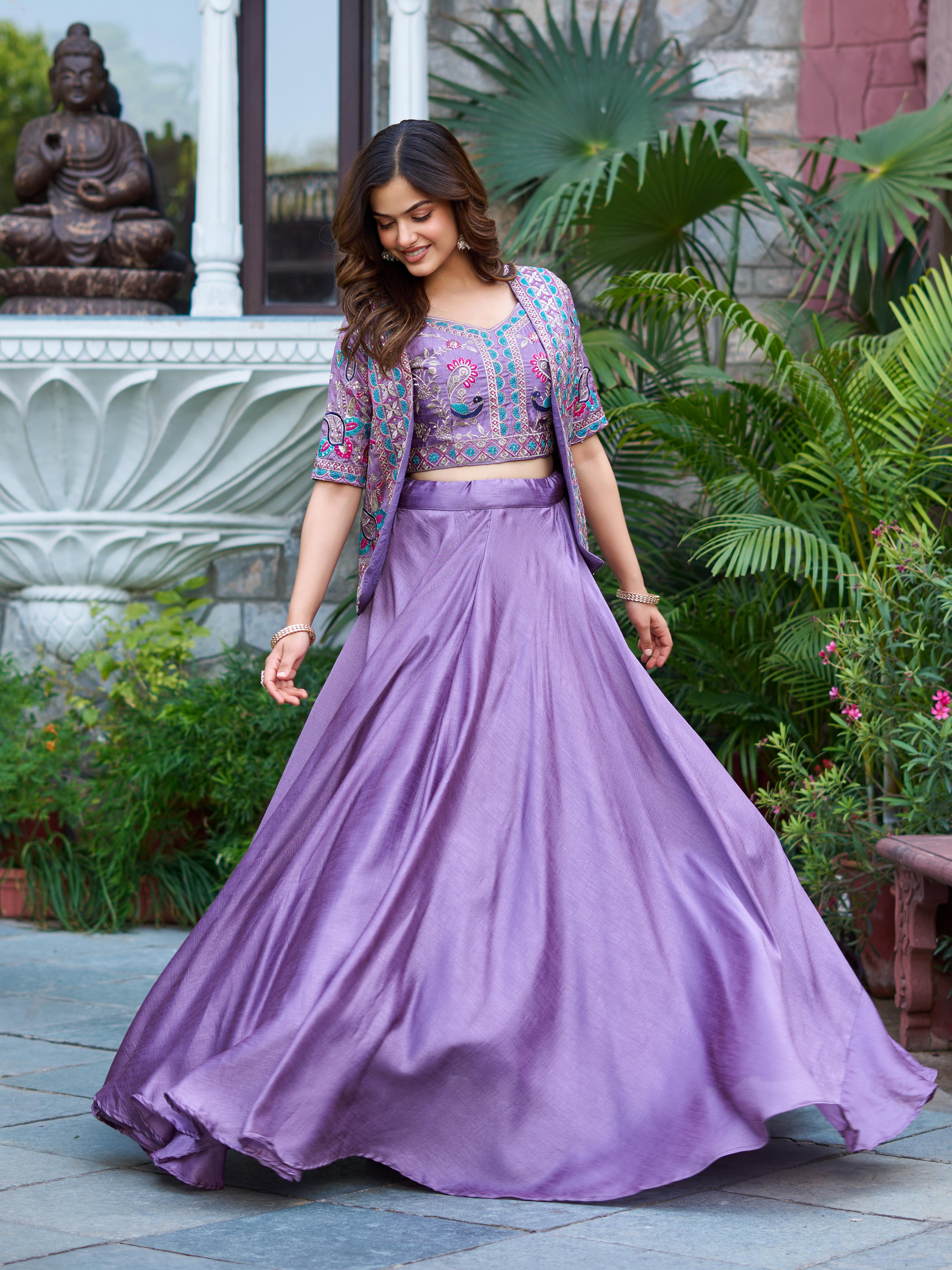 Woman in a purple traditional outfit standing outdoors with greenery and a statue in the background