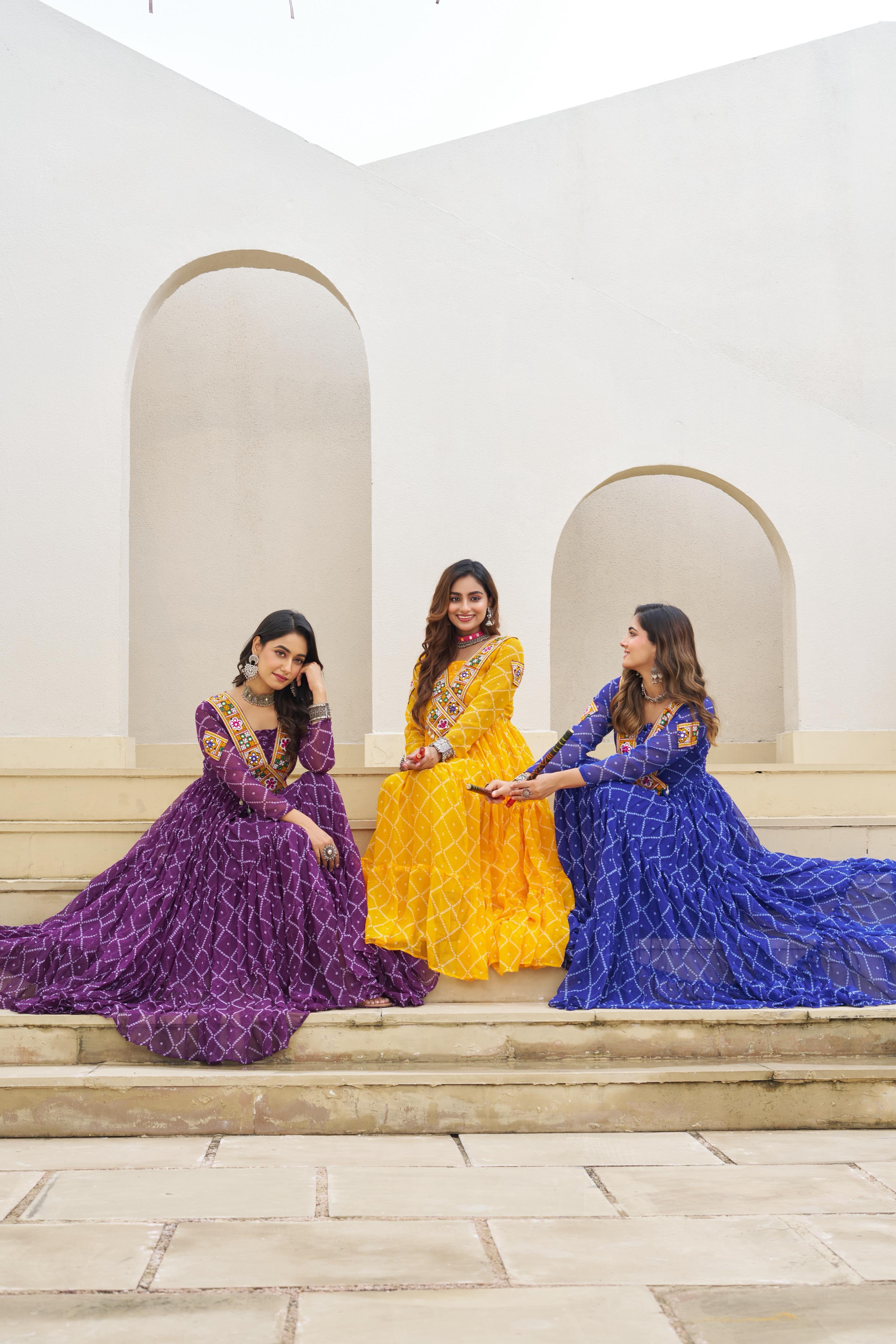 Three women in colorful traditional dresses sitting on steps with a white architectural background