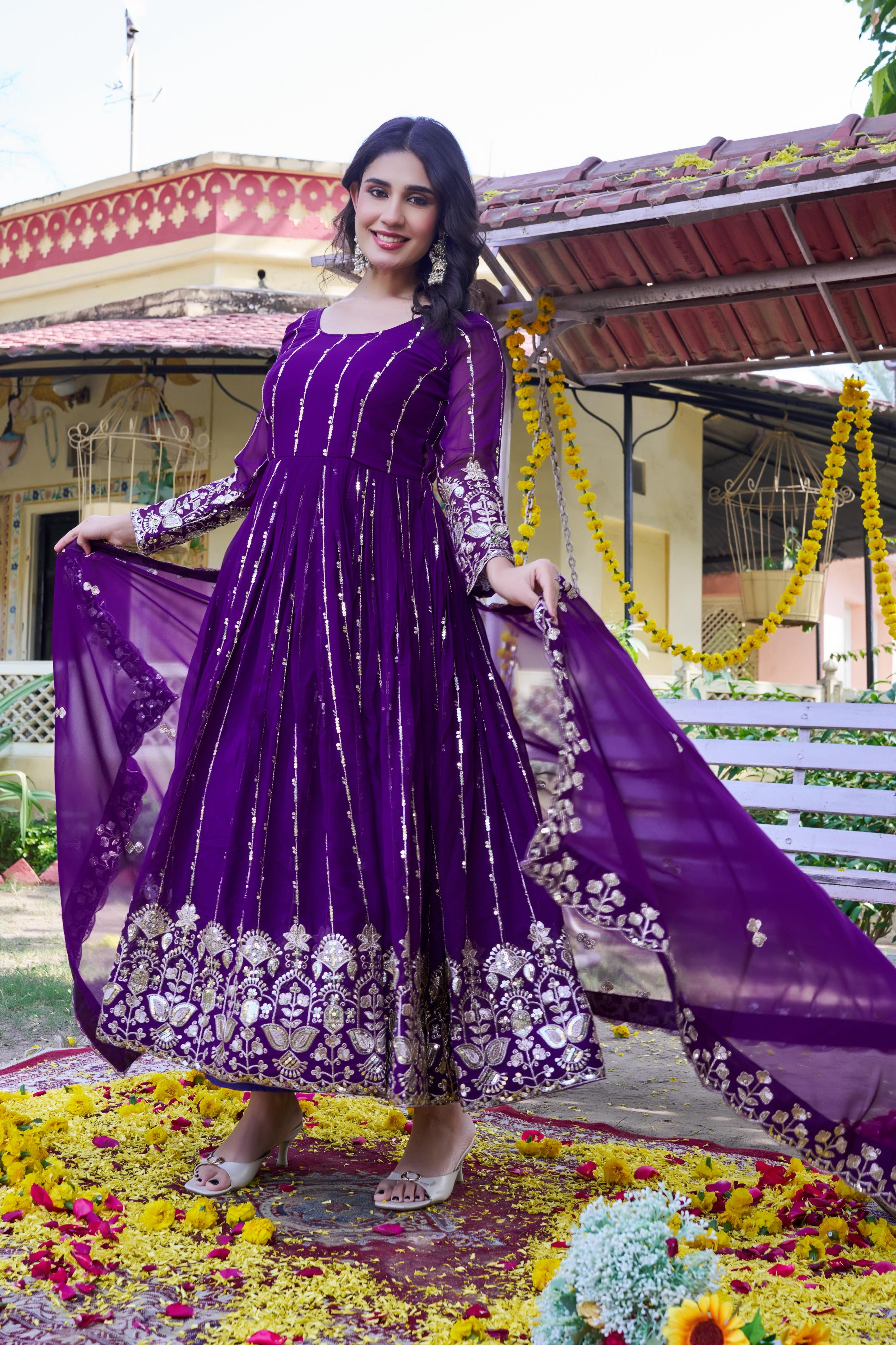 Woman in a purple traditional outfit standing on a decorated ground with flowers.