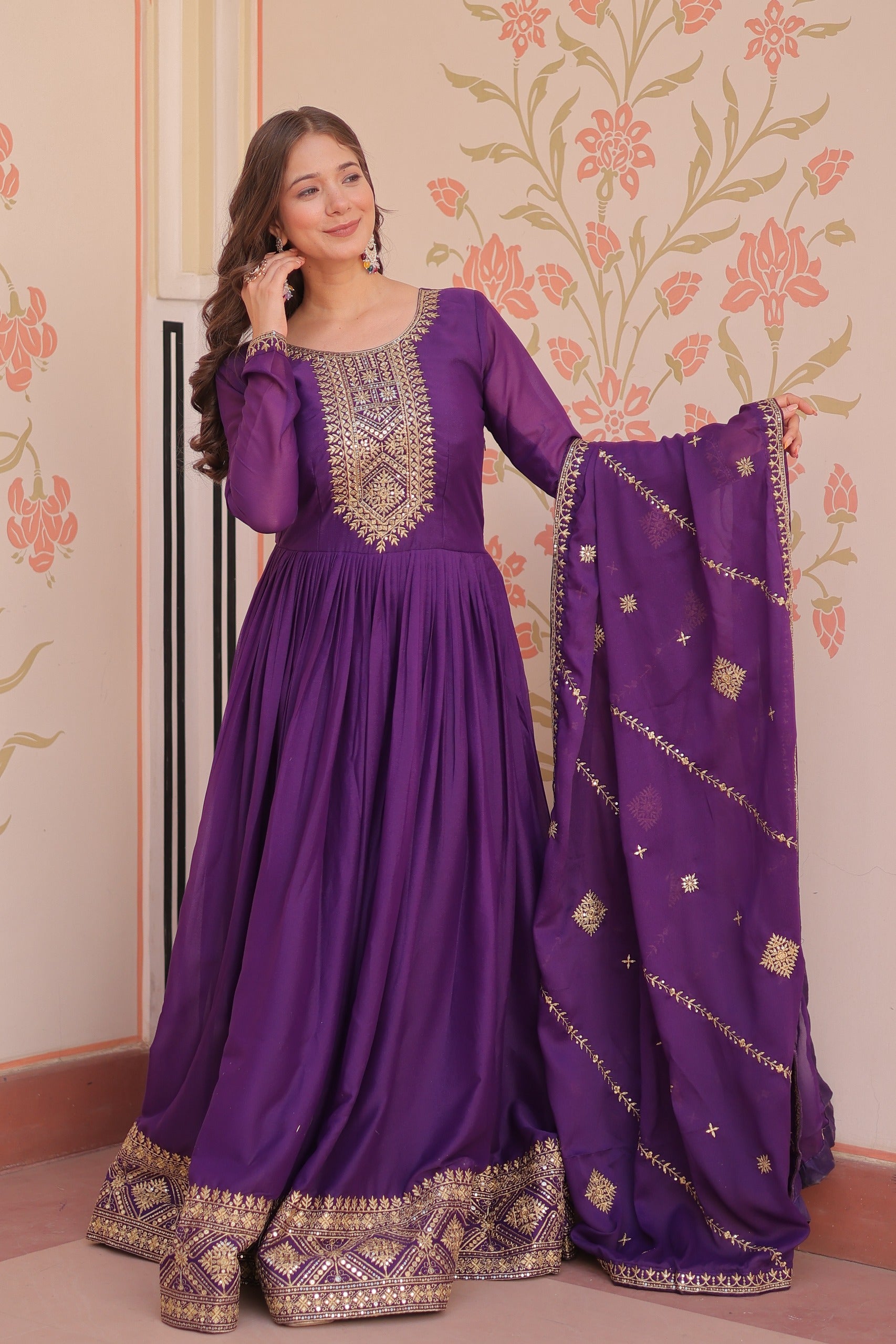 Woman wearing a purple traditional gown with gold embroidery in a decorated room.