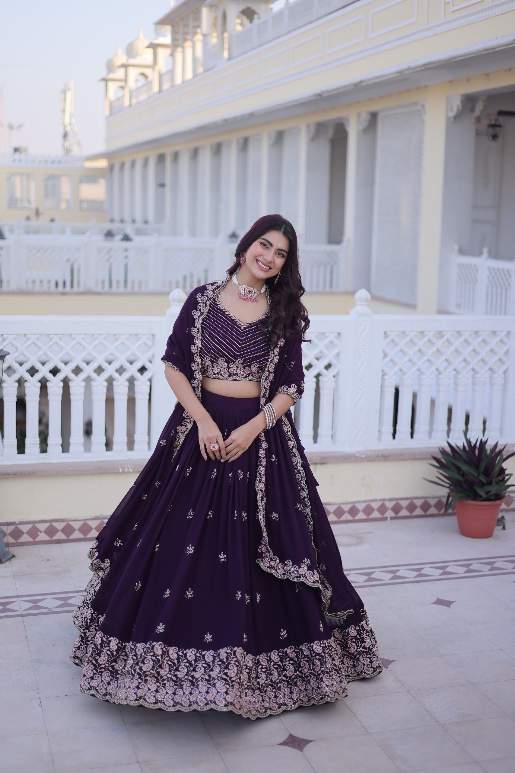 Woman in a dark purple traditional outfit standing on a balcony with white railings.