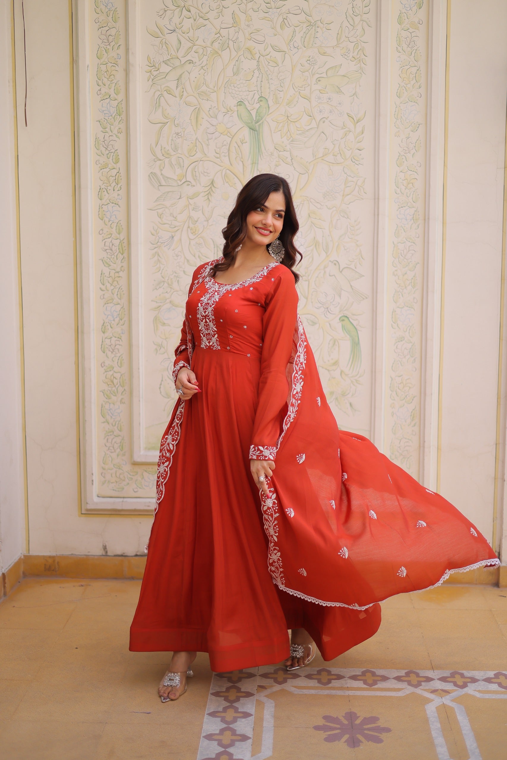 Woman in a red traditional outfit with white embroidery standing in a decorated room.