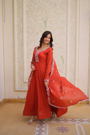 Woman in a red traditional outfit with white embroidery standing in a decorated room.