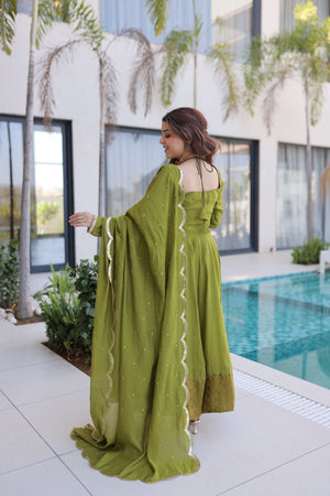 Woman in a green dress standing by a pool with modern building and plants in the background