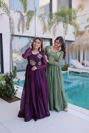 Two women in long dresses standing by a poolside with a modern building in the background.