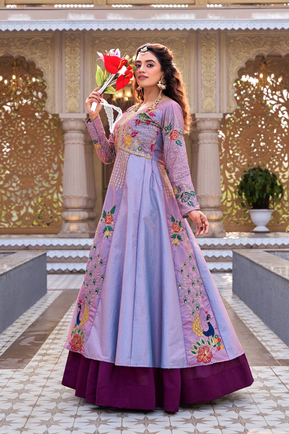 Woman in a traditional outfit with floral patterns holding a red flower in an ornate setting.