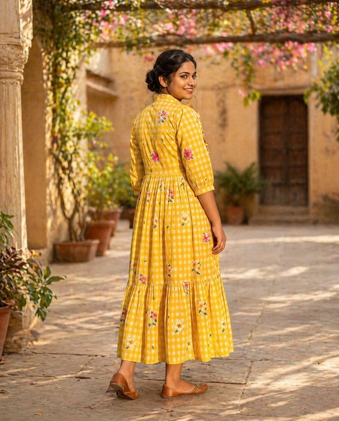 Woman in a yellow dress with floral patterns standing in a sunlit courtyard.