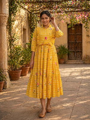 Woman in a yellow checkered dress with floral patterns standing in an outdoor setting.