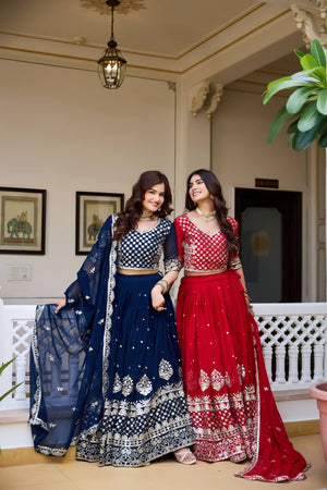 Two women in traditional outfits standing indoors with decorative elements in the background.