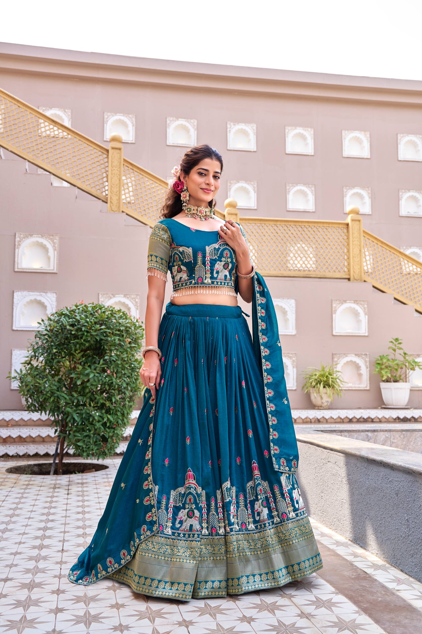 Woman in a traditional teal outfit standing in front of a building with decorative elements.