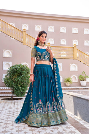 Woman in a traditional teal outfit standing in front of a building with decorative elements.