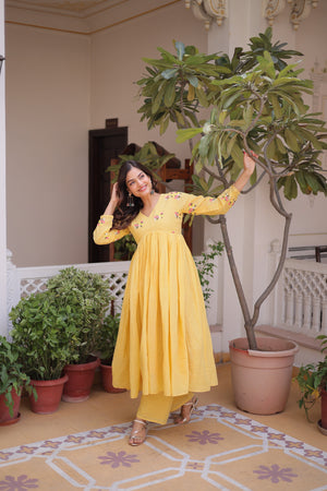 Woman in a yellow dress standing in a room with plants and decorative tiles.