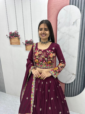 Woman in a maroon traditional outfit with floral patterns in a decorated indoor setting.