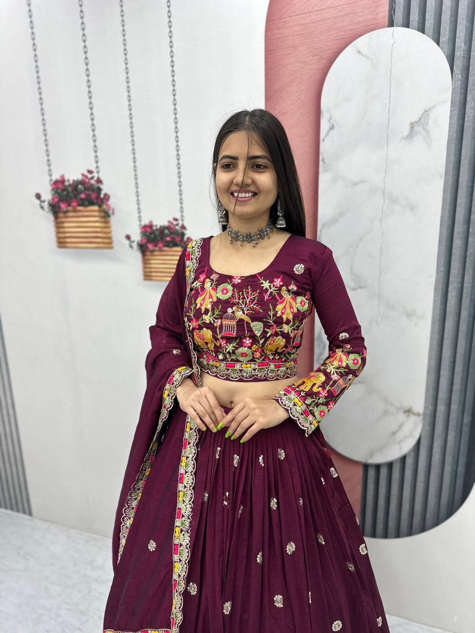 Woman in a maroon traditional outfit with floral patterns in a decorated indoor setting.