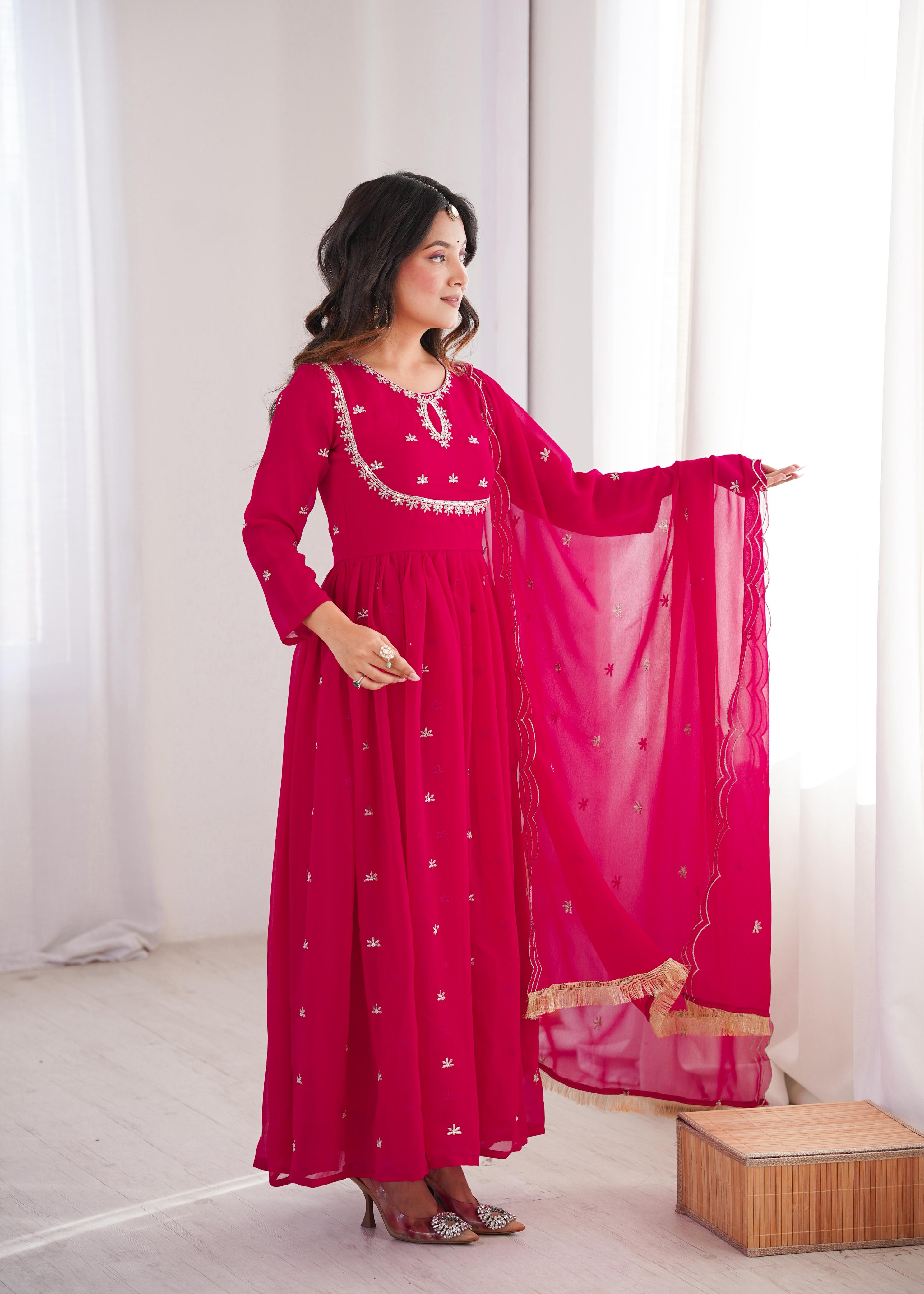 Woman wearing a pink traditional outfit with white patterns in a bright room.
