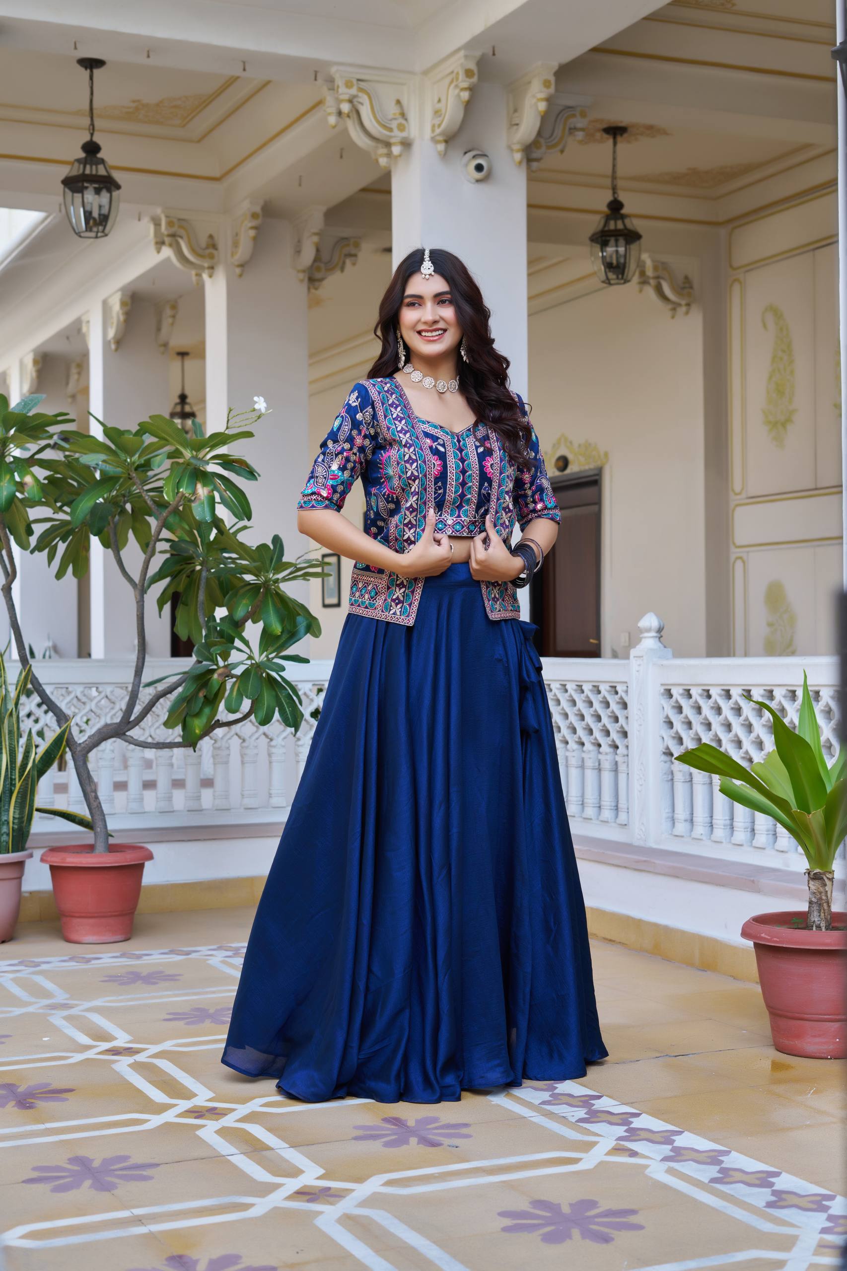 Woman in a blue traditional outfit standing in an ornate indoor setting with plants.