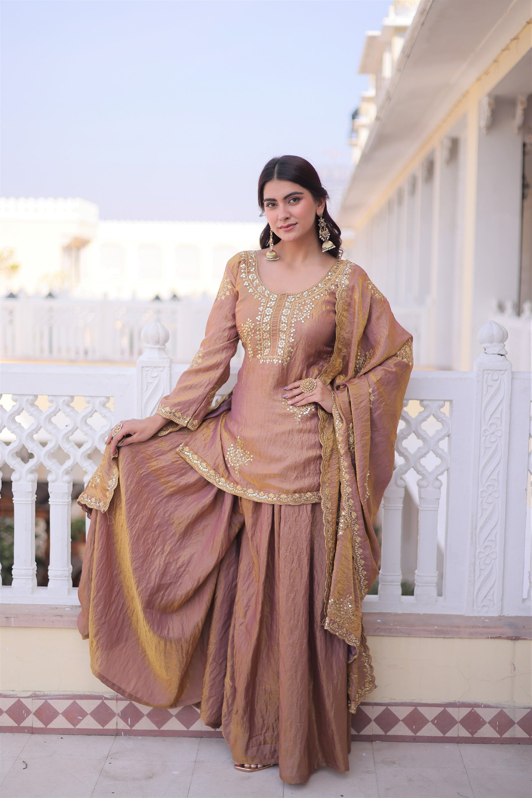 Woman in a traditional outfit standing on a balcony with a white railing and building in the background.