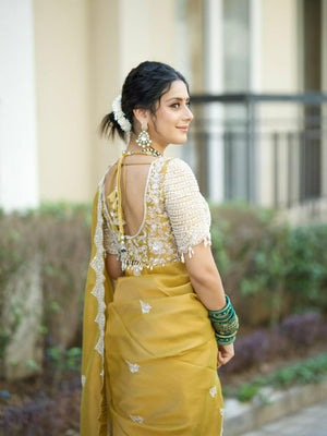 Woman in a yellow saree with a white blouse, standing outdoors.